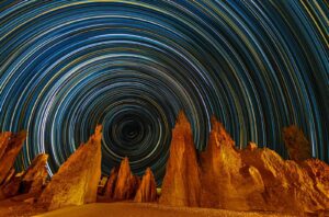 Star trails circle above desert rock formations.