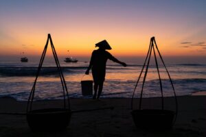 Fisherman with buckets at sunrise on a beach